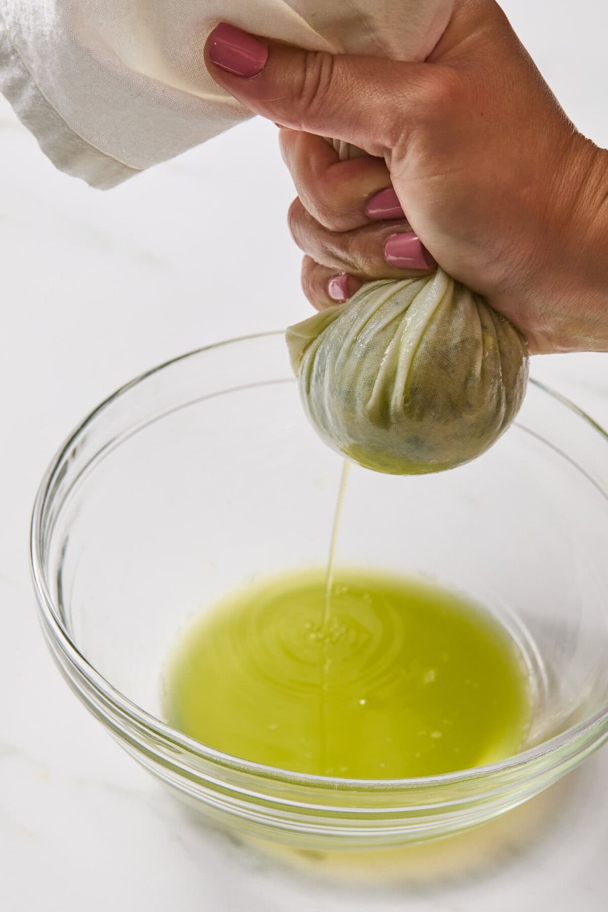 A hand squeezes a cloth pouch of greens over a glass bowl, releasing bright green liquid onto the bowl's surface-a vibrant step in crafting moist zucchini brownies.