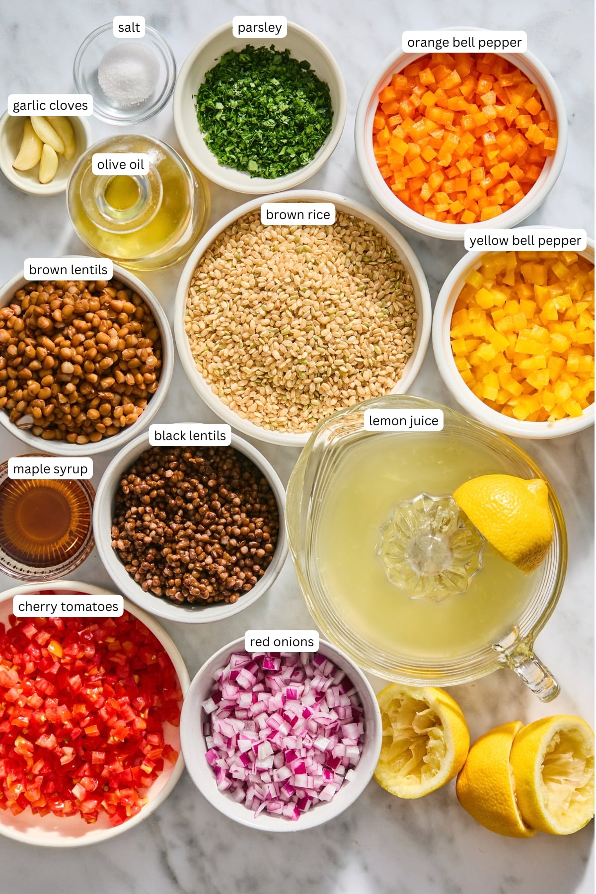 An overhead view of chopped vegetables, lentils, rice, lemon juice, olive oil, maple syrup, and seasonings in bowls on a marble surface, each ingredient labeled with text-perfect for assembling a vibrant lentil rice salad.