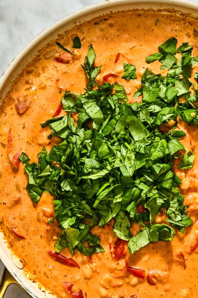 Creamy Tuscan white beans in a tomato sauce skillet topped with a generous pile of chopped fresh basil.