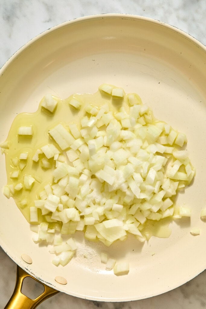 Diced white onions for creamy Tuscan white beans sautéing in oil in a light-colored skillet.