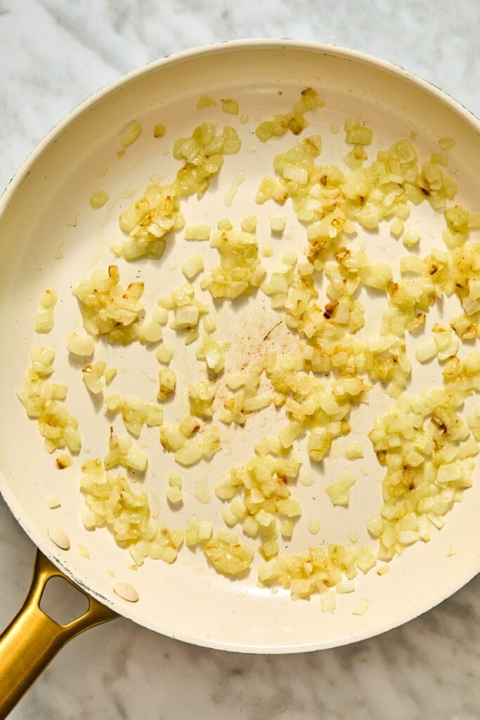 Diced onions sautéing in a light-colored skillet for creamy Tuscan white beans.