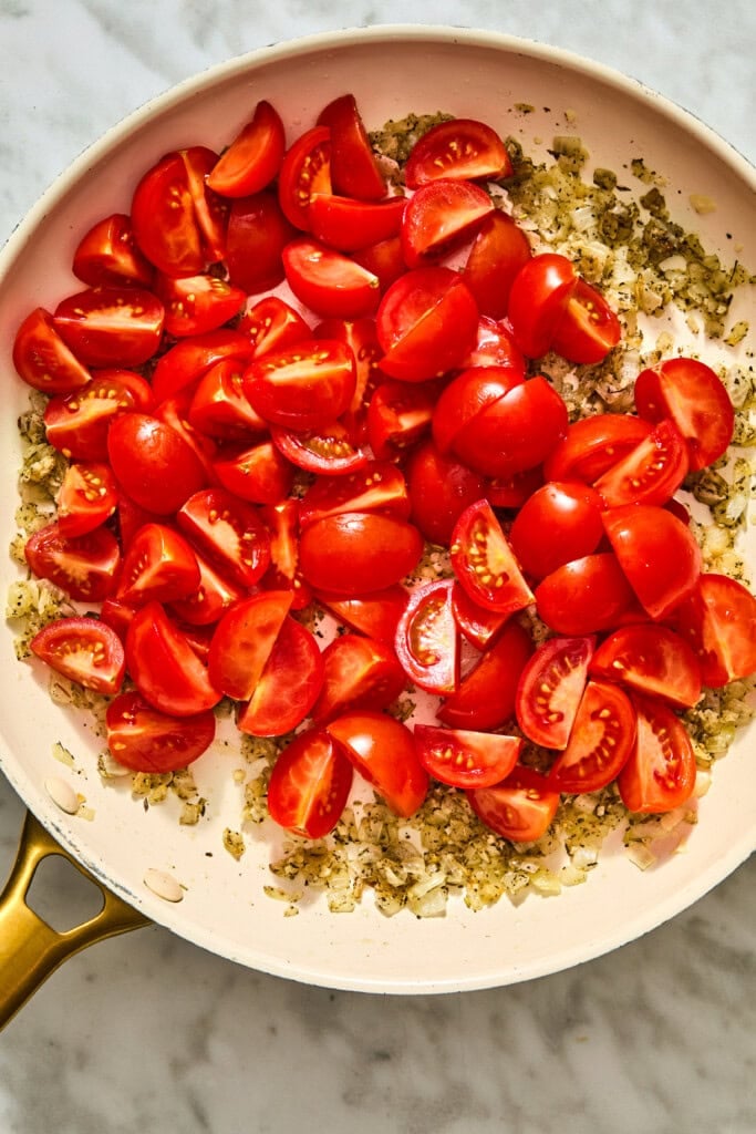 A skillet of creamy Tuscan white beans with halved cherry tomatoes resting on a bed of sautéed onions and herbs.