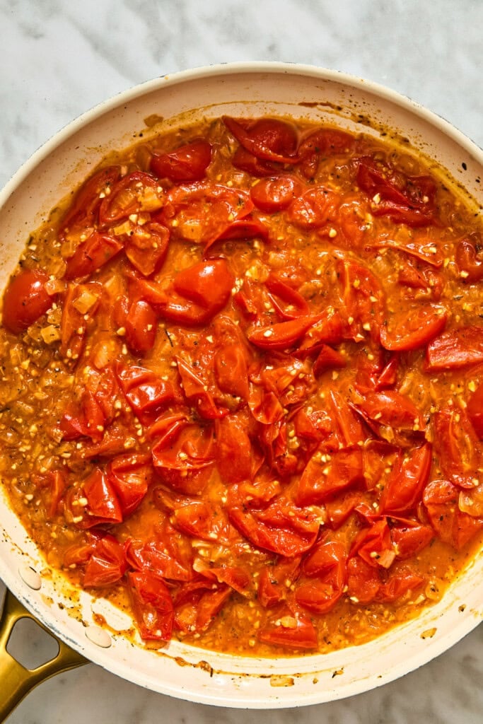 A skillet filled with creamy Tuscan white beans, cherry tomatoes, and aromatics simmering in a red sauce.