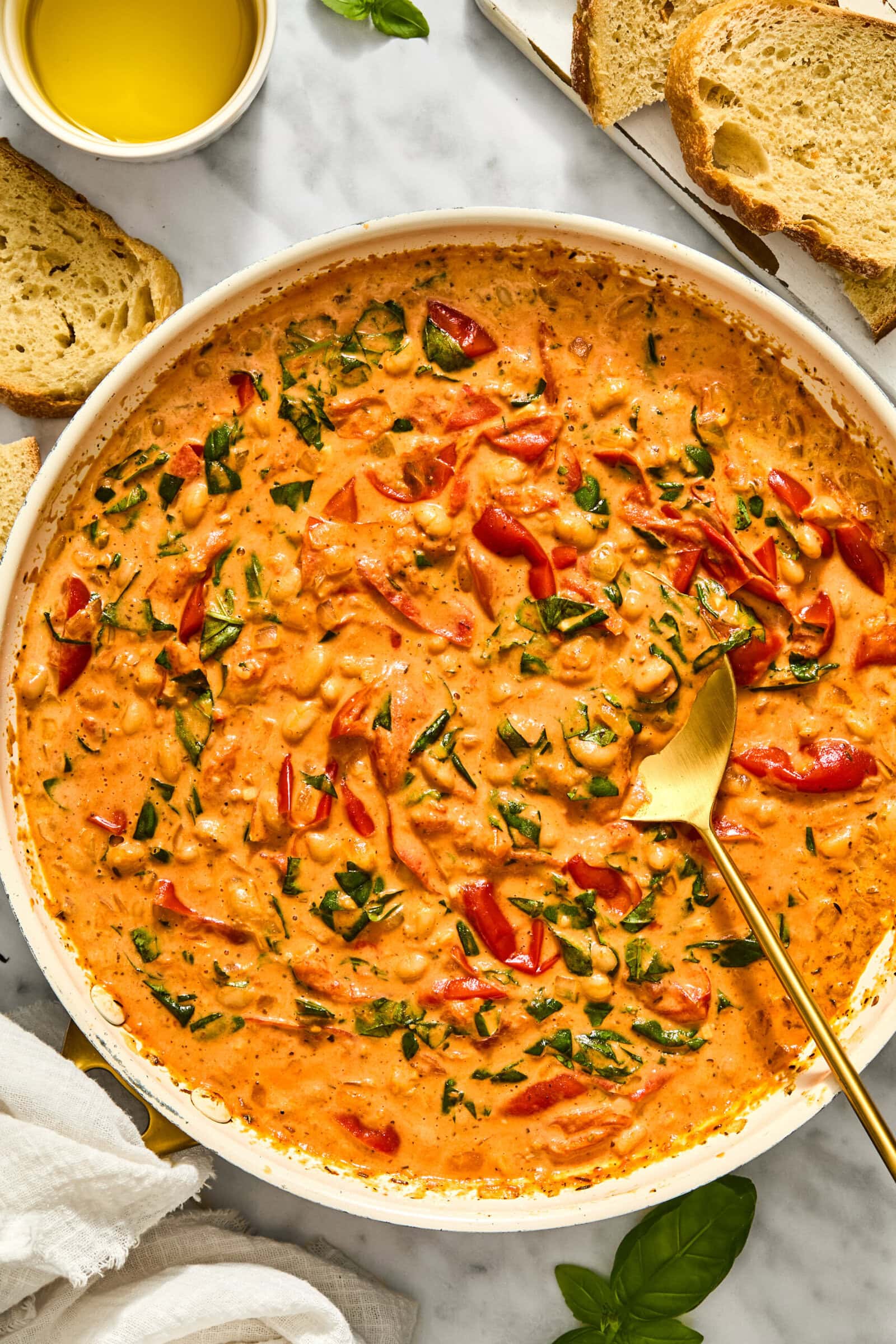 A skillet of creamy Tuscan white bean stew with spinach, served with slices of bread and a small bowl of oil.