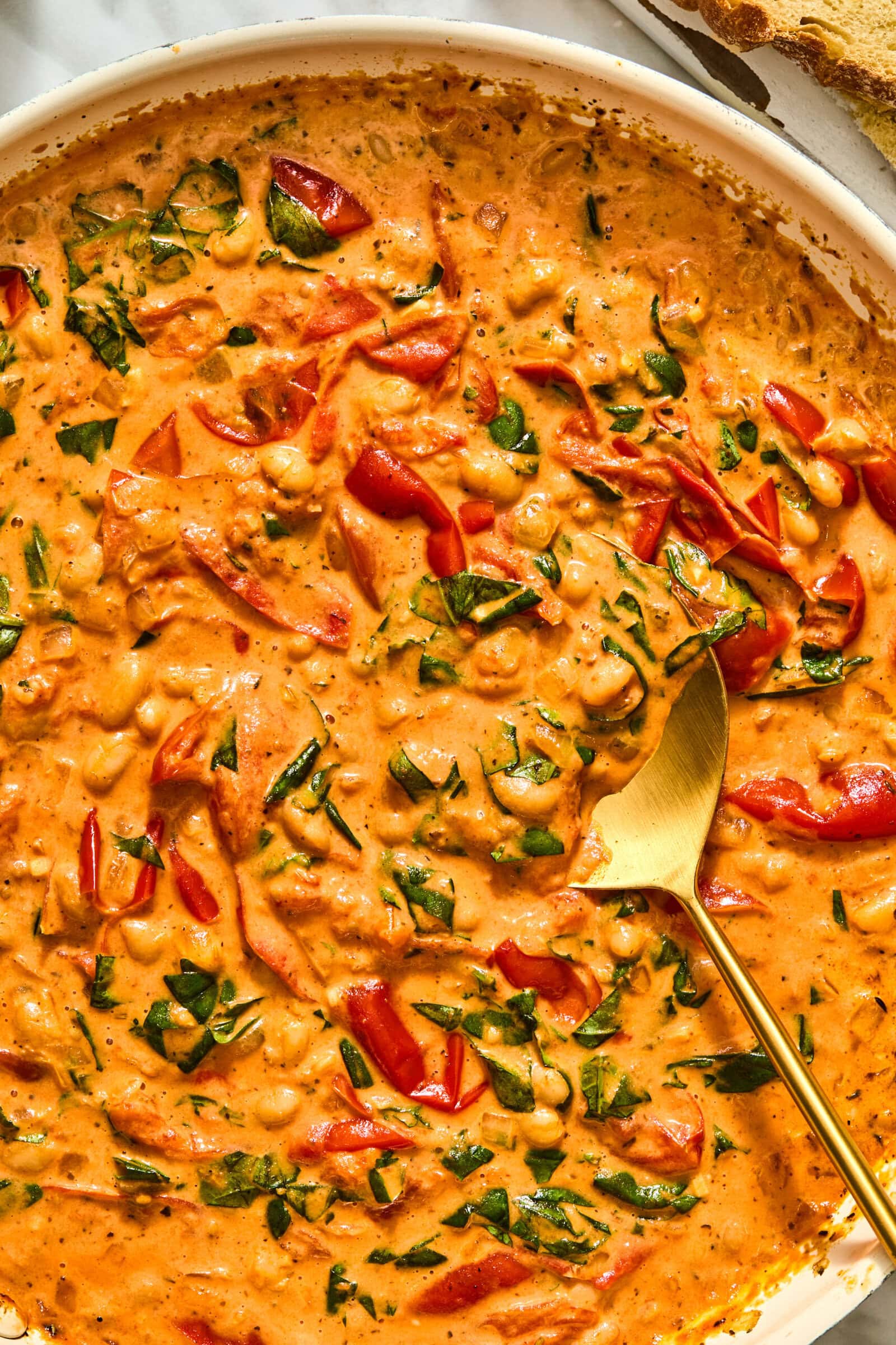 Creamy Tuscan-style tomato stew with chickpeas, red bell peppers, and greens in a pan with a golden serving spoon.