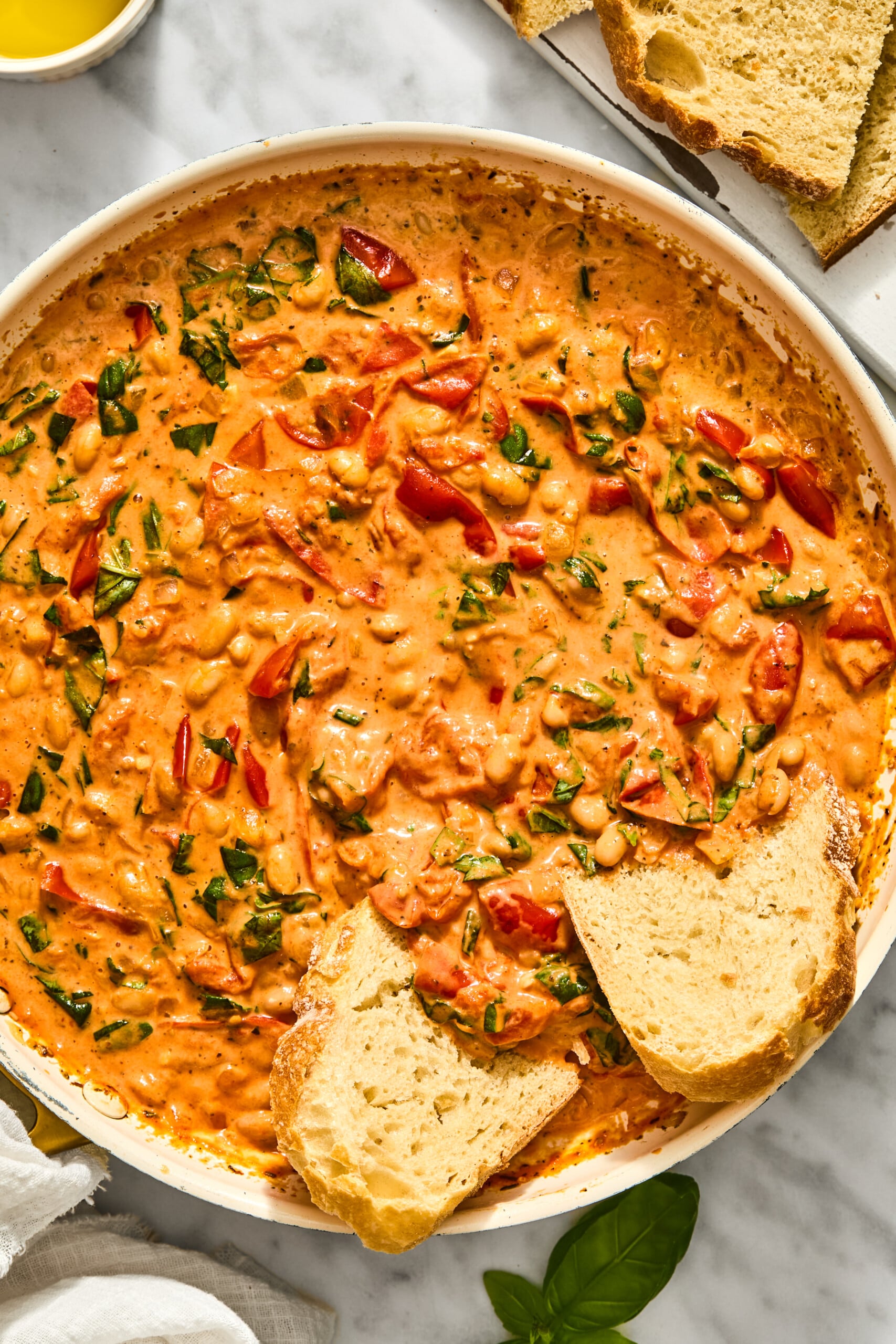 A skillet of creamy Tuscan white bean stew garnished with fresh basil, served with slices of crusty bread.