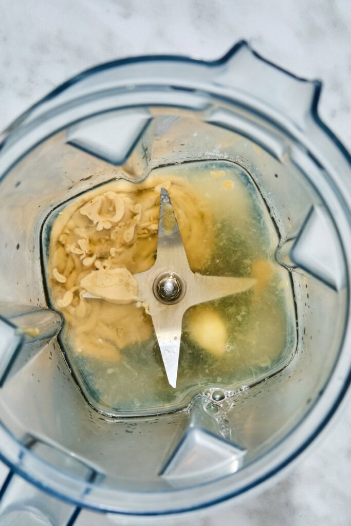 Top-down view inside a blender containing a beige high-protein chickpea salad mixture and clear liquid around the blades.