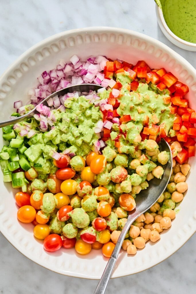 A bowl of high-protein chickpea salad with cherry tomatoes, diced red onion, bell peppers, and cucumbers, drizzled with a green herb dressing.
