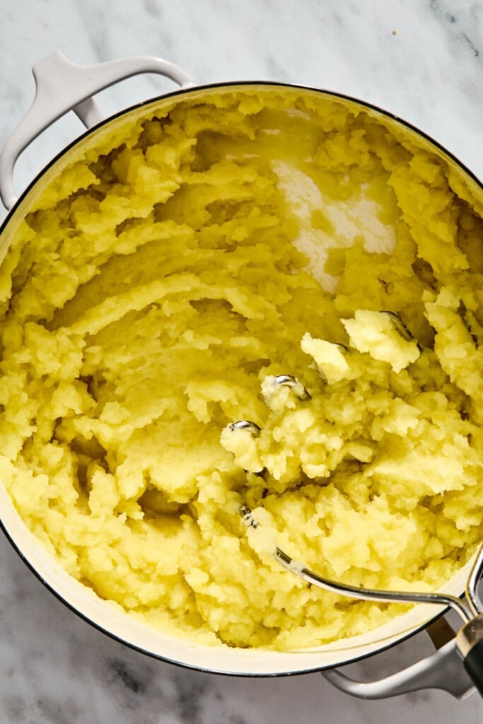 Mashed potatoes in a white pot with a potato masher.