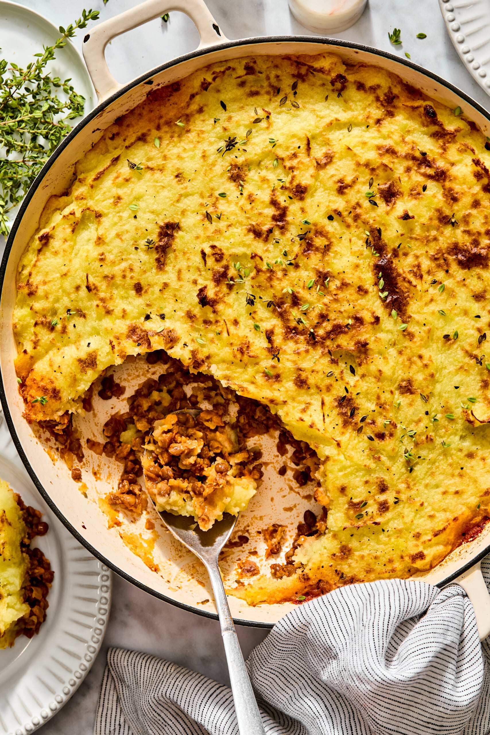 Shepherds pie in a shallow pan with a metal spoon scooping out a serving, topped with fresh herbs.