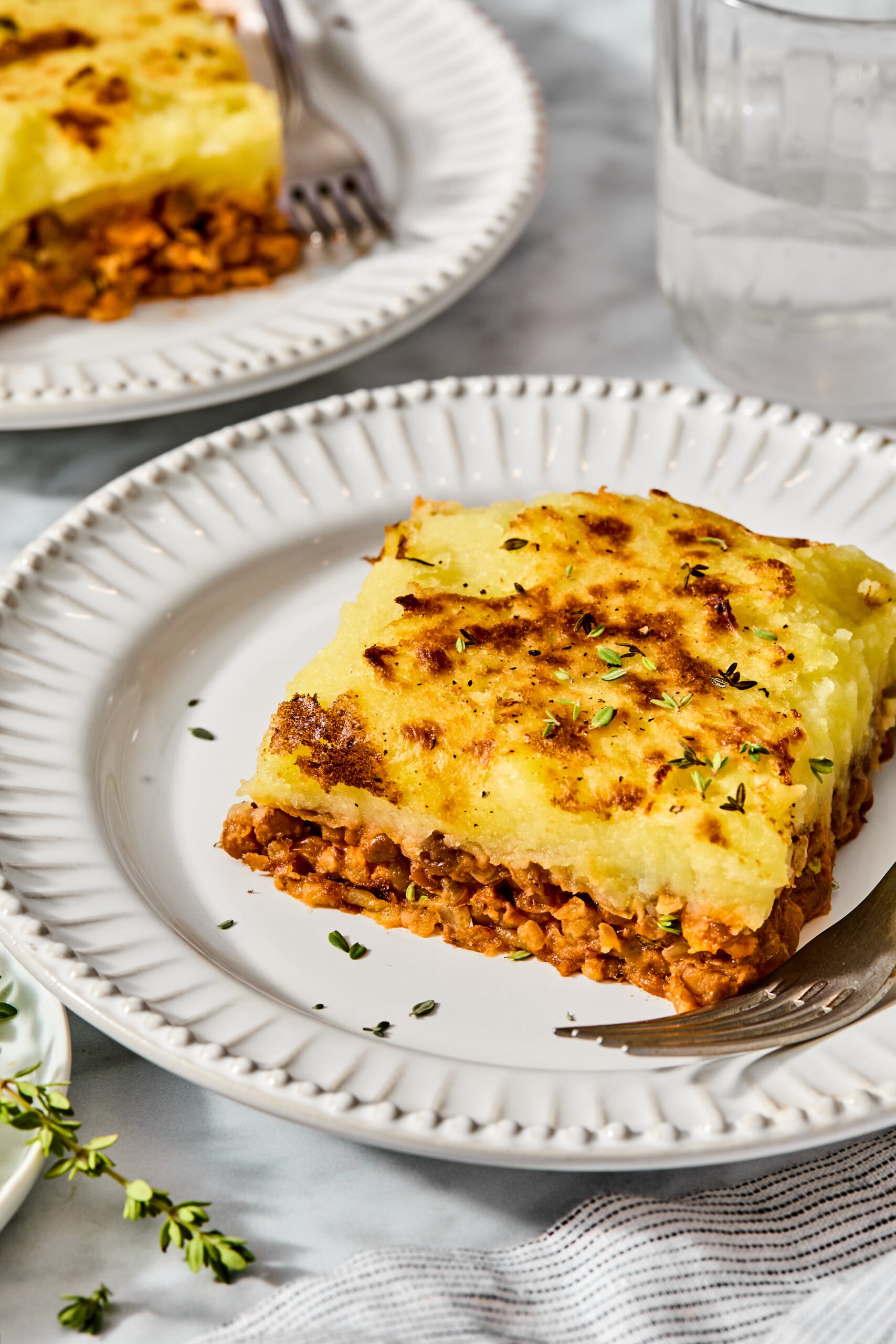 A serving of shepherds pie with a golden mashed potato topping and a savory meat base on a white plate with a fork.