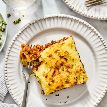A serving of shepherds pie with a mashed potato topping on a white plate, with a fork breaking into the meat and lentil filling.