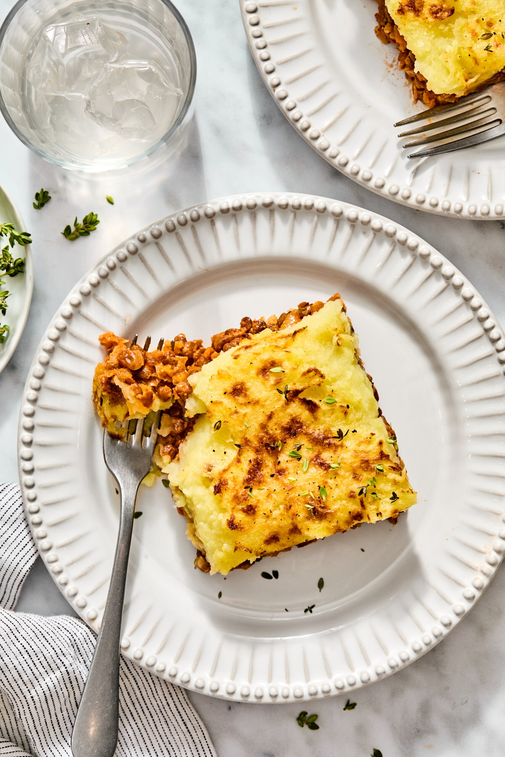 A serving of shepherds pie with a mashed potato topping on a white plate, with a fork breaking into the meat and lentil filling.