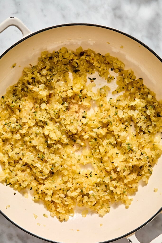 Finely diced onions and herbs sautéing in a shallow enameled pan.