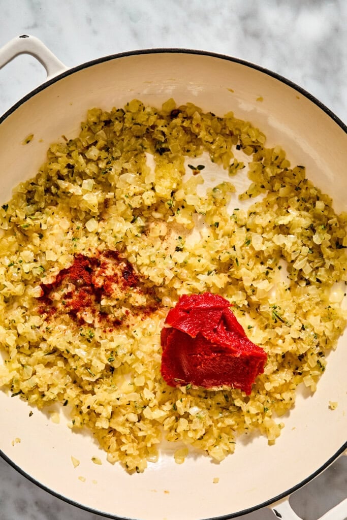 A pan of sautéed onions with a dollop of red tomato paste and a dusting of reddish spice.