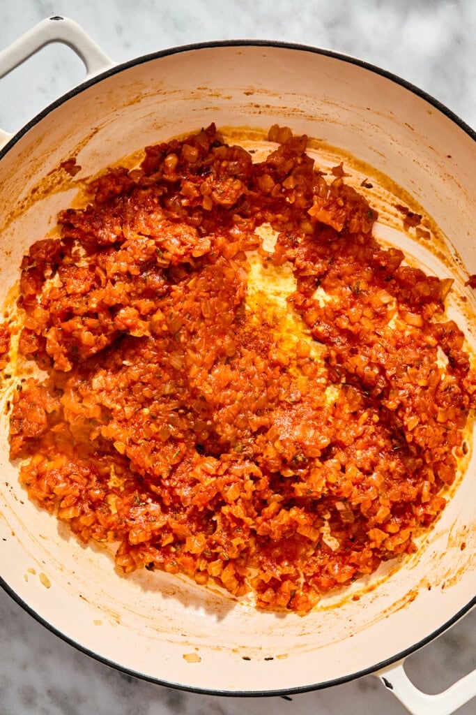 A thick, red tomato and onion sauce cooking in a large white enameled cast iron pot.