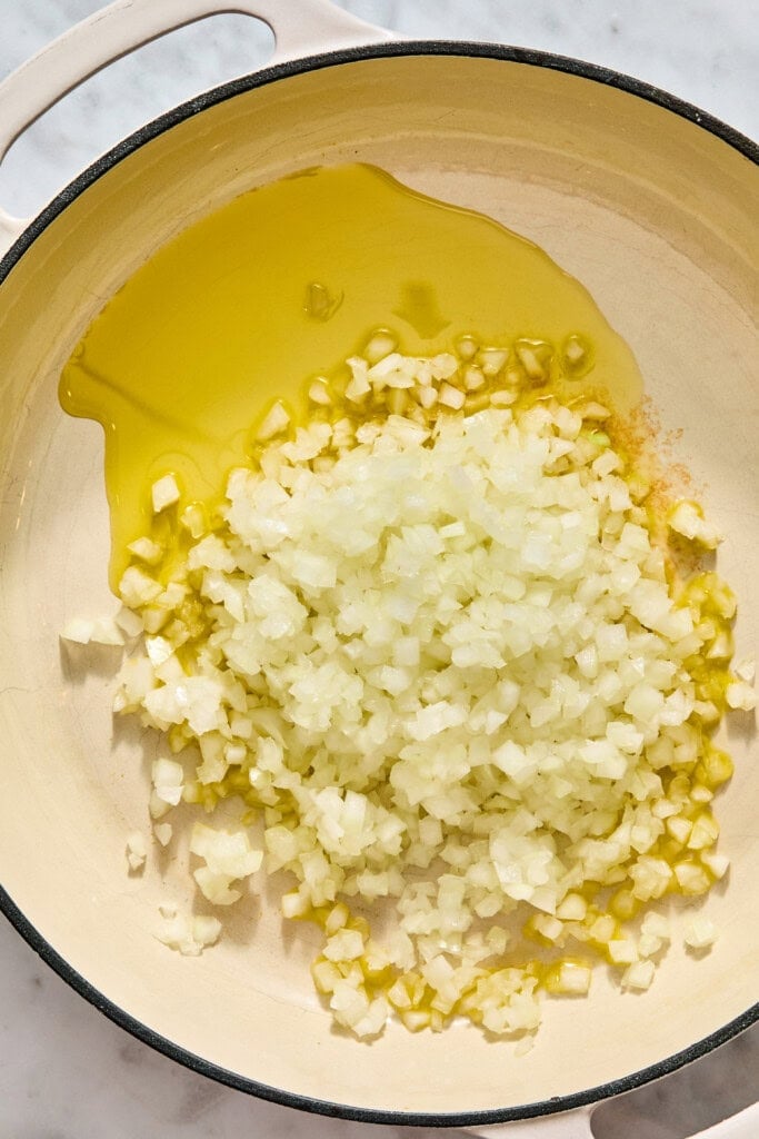 Diced onions sautéing in olive oil in a wide enameled pan.