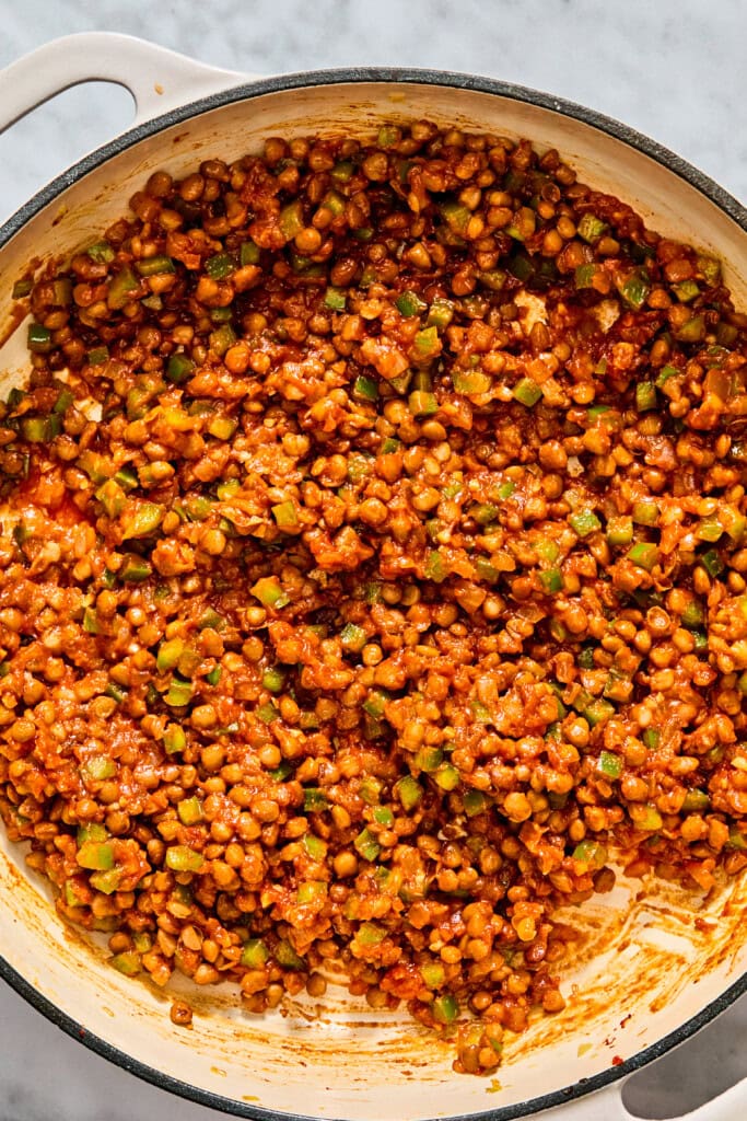 A large skillet filled with a mixture of lentils, diced green peppers, and red tomato sauce.