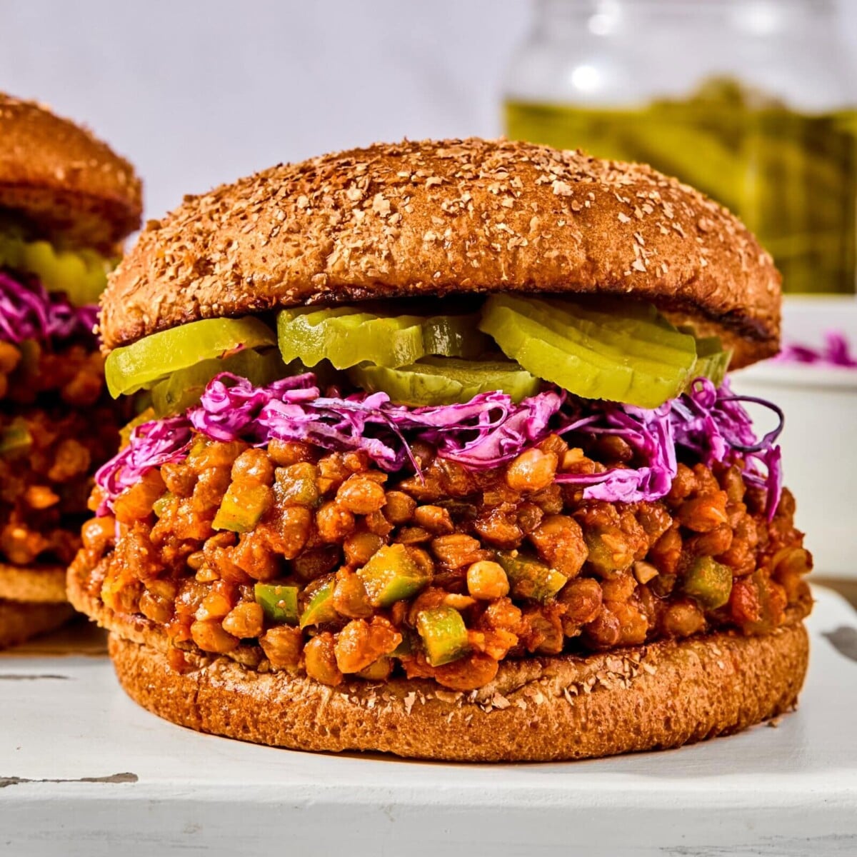 A sloppy joe sandwich on a seeded bun, topped with purple cabbage slaw and pickle slices.