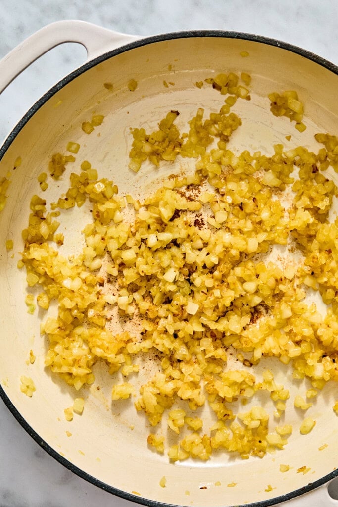 Finely chopped yellow onions sautéing in a wide enameled skillet.