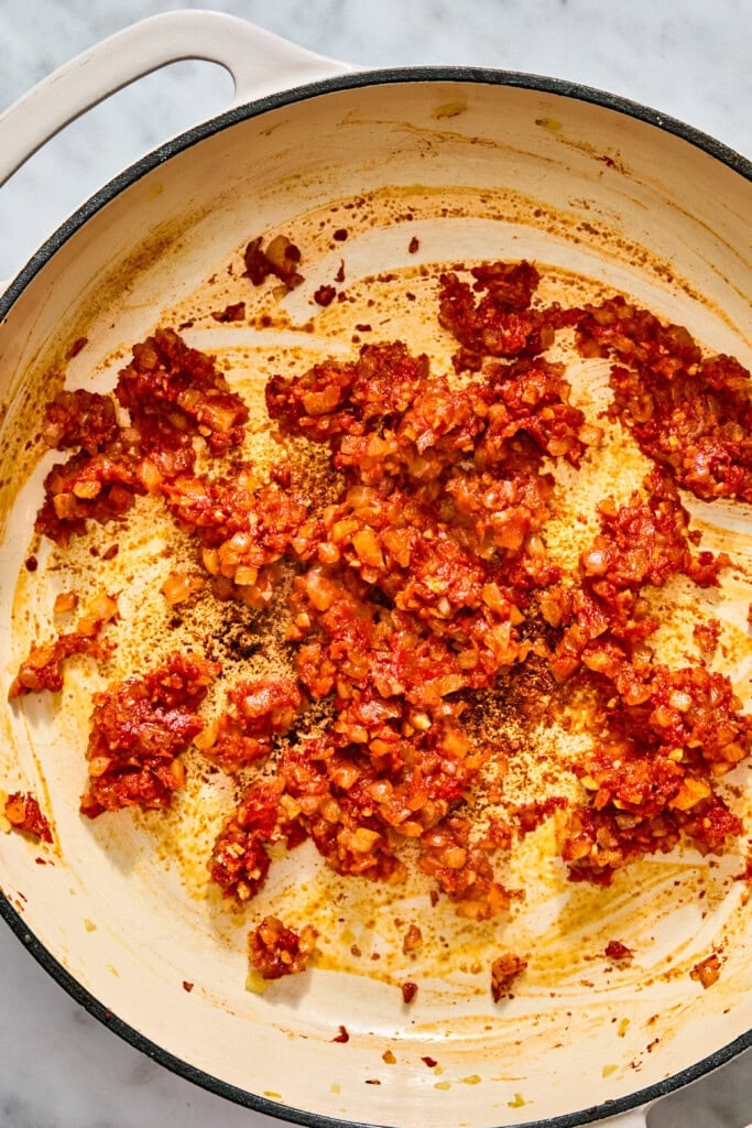 Sautéed chopped onions and tomato paste cooking in a shallow enamel skillet.