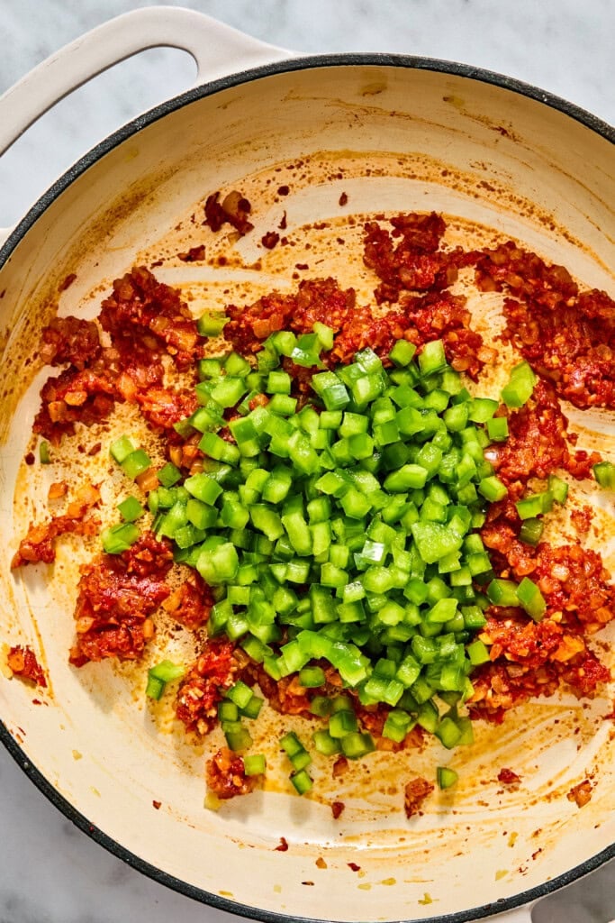 Diced green bell peppers added to a skillet with sautéed red aromatics.