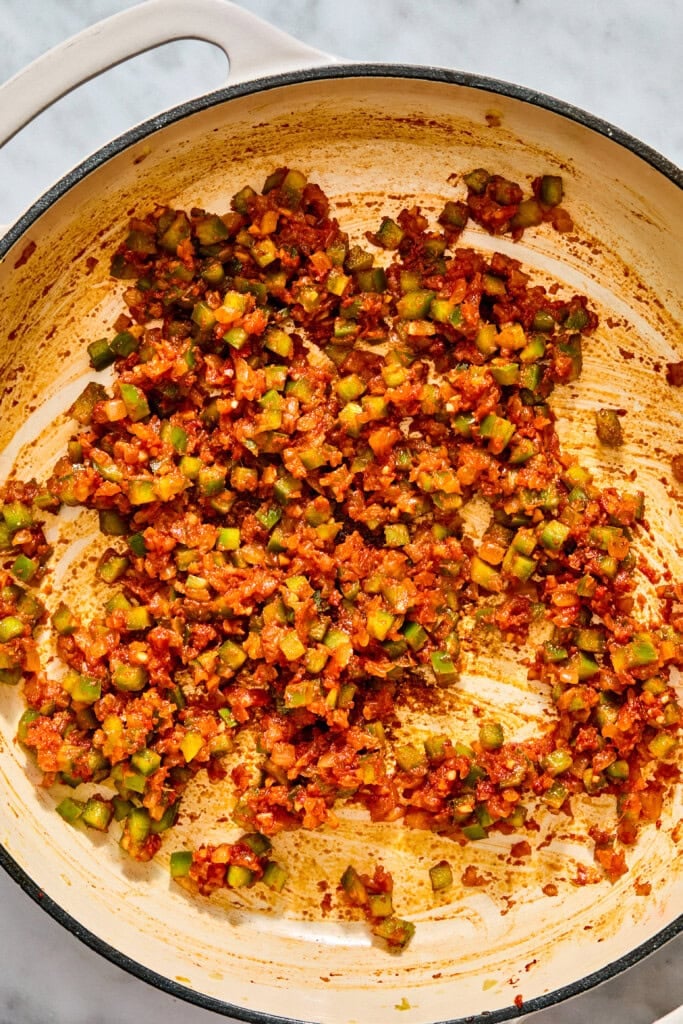 Finely diced vegetables sautéed in a red sauce in a light-colored enameled skillet.