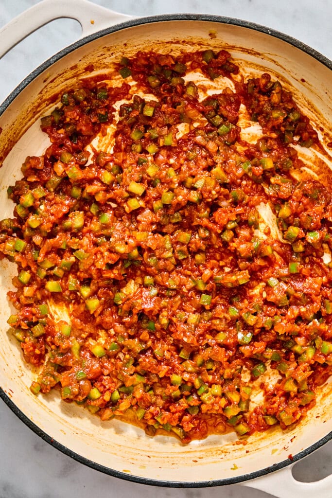 A skillet filled with a cooked mixture of sautéed green vegetables in a thick, red tomato-based sauce.