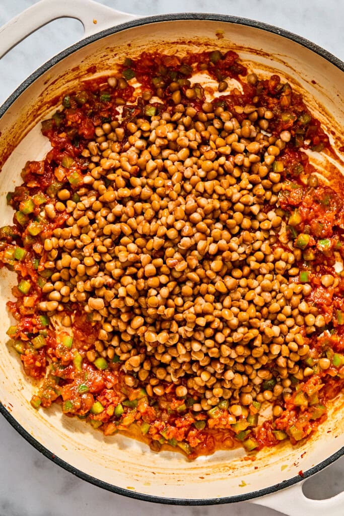 Lentils cooking in a skillet with a tomato-based sauce and chopped vegetables.