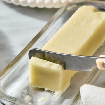 A knife cuts through a stick of butter on a glass dish.
