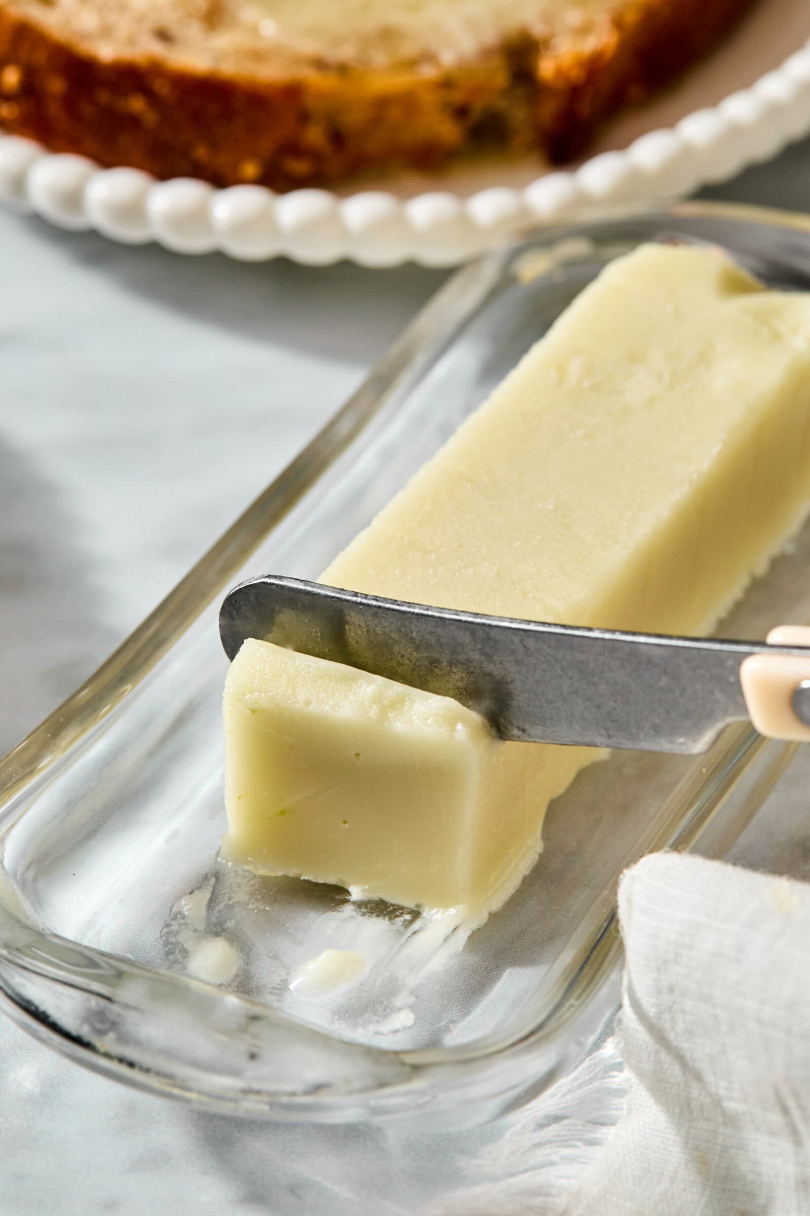 A knife cuts through a stick of butter on a glass dish.