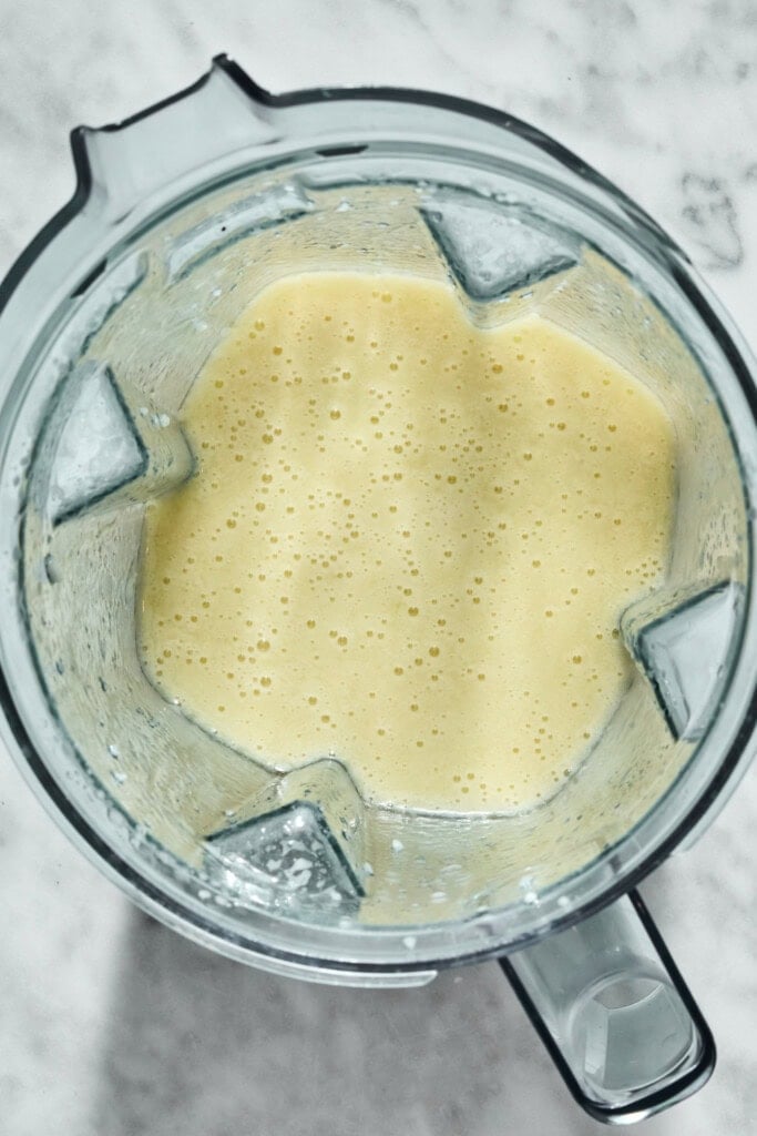 A blender pitcher filled with a blended yellow smoothie.
