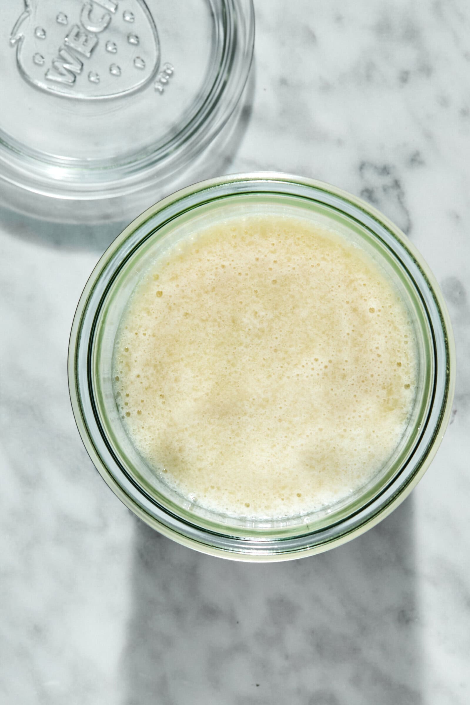 A glass jar filled with a creamy, pale yellow liquid next to its open lid.